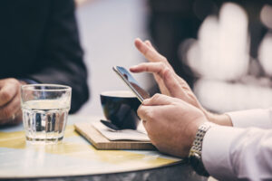 Male hands texting with the phone and couple of cups of coffee in the background